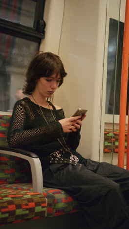 Vertical-Video-Shot-Of-Alternative-Style-Woman-Using-Mobile-Phone-Sitting-On-London-Underground-Train-In-Real-Time-1