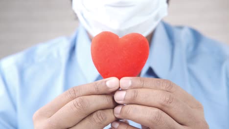 person with mask holding a red heart