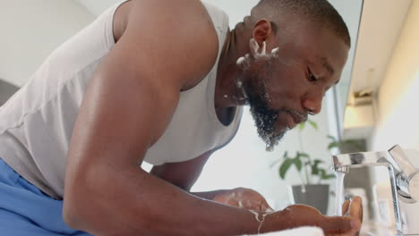 washing face in bathroom, strong and fit african american man enjoying self-care
