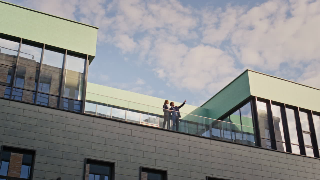 Business partners standing balcony modern office building. Businessman pointing