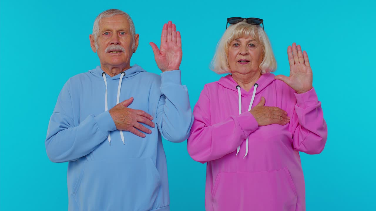 Coppia di anziani nonni sinceri e responsabili che alzano le mani per giurare e dire la verità.