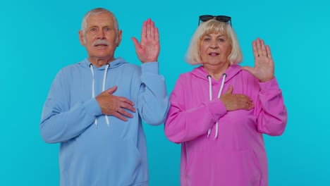 Sincere-responsible-senior-couple-man-woman-grandparents-raising-hands-to-take-oath,-tell-truth