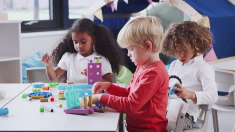 white infant school boy using educational construction toys with his classmates, close up