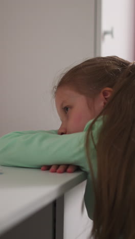 thoughtful little girl lies leaning on desk with school supplies in children room. upset schoolgirl tired of complicated lessons in school sits at table