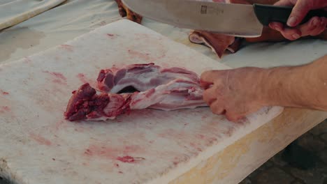 close up of man slicing pork skin with knife on stained cutting board during meat processing
