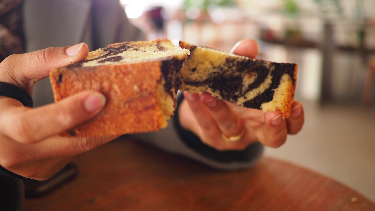 Close-up of Hands Breaking a Slice of Marble Cake