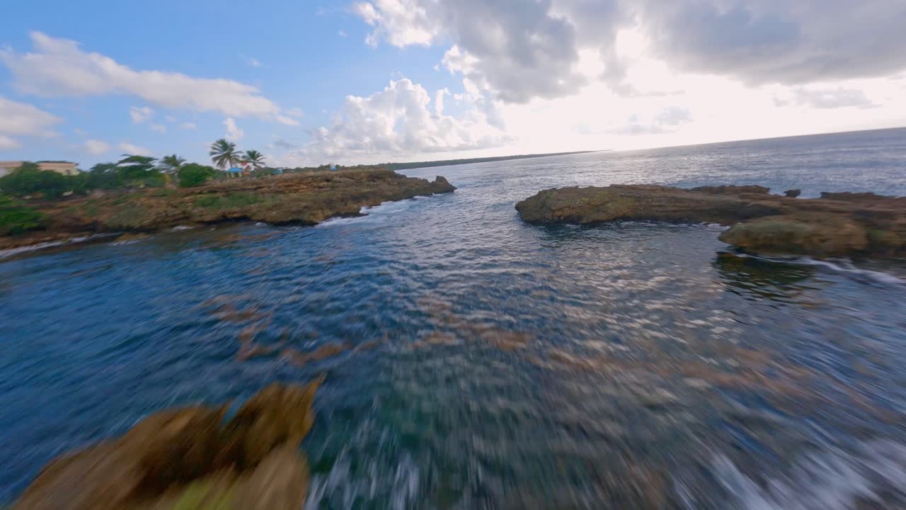 vuelo aéreo fpv a lo largo de la costa rocosa y el agua azul clara del mar caribe - toma ascendente con toma panorámica sobre el campo verde en crecimiento de la república dominicana