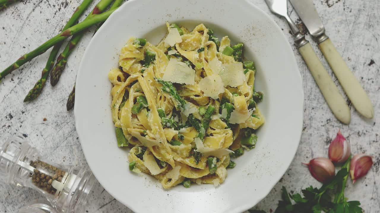 크리미한 리코타 치즈 소스와 아스파라거스를 곁들인 홈메이드 탈리아텔레 파스타는 흰색 세라믹 접시에 제공됩니다.