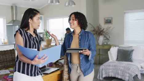 Diverse-female-friends-talking,-using-tablet,-working-at-home,-in-slow-motion