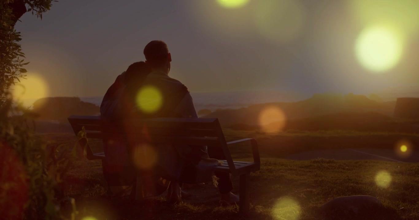 Film couple sitting seat facing sun as bokeh shifting showing silhouettes, one leaning for warmth