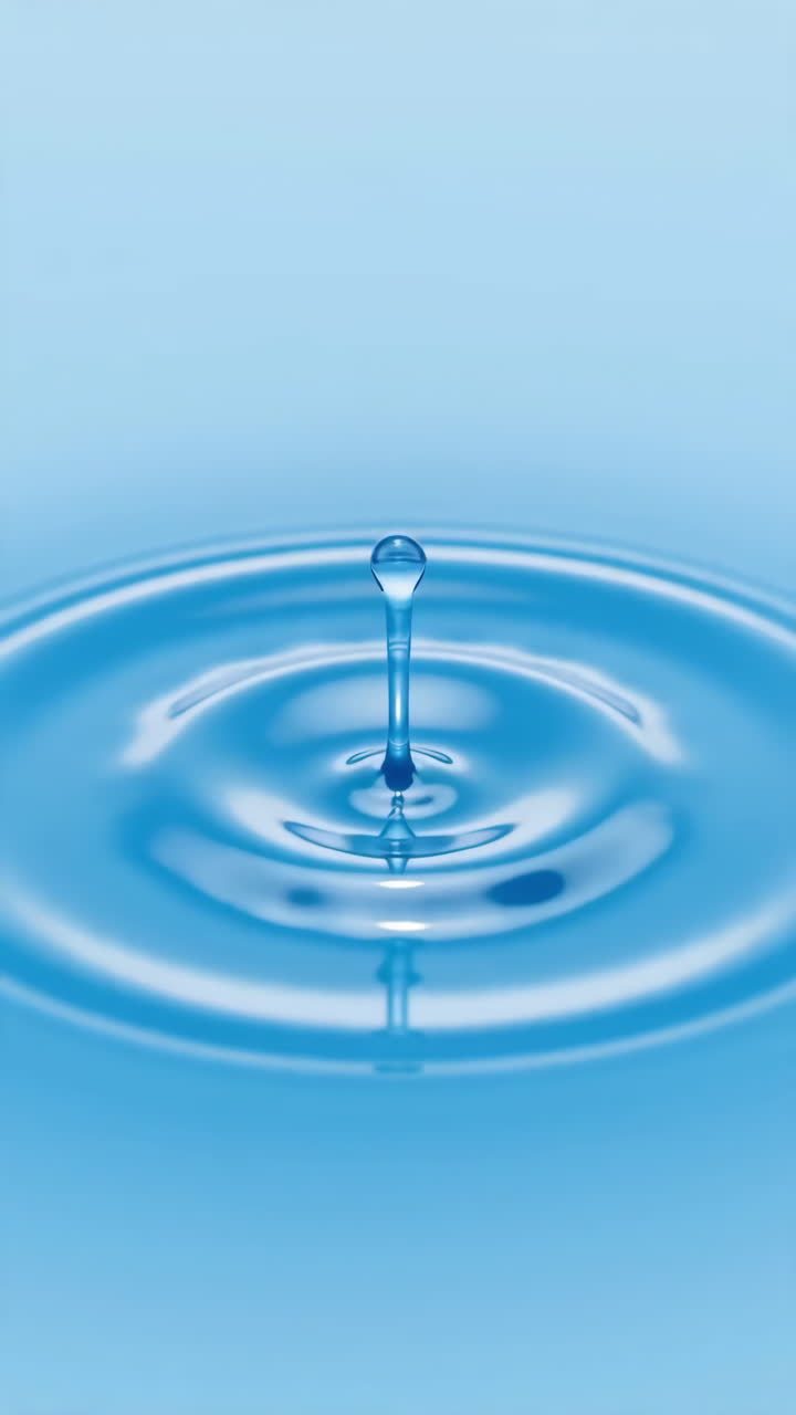 Blauer Wassertropfen erzeugt einen Kronenspritzer in Hochgeschwindigkeits-Nahaufnahme, konzentrische Wellen breiten sich über einer glänzenden Oberfläche aus.