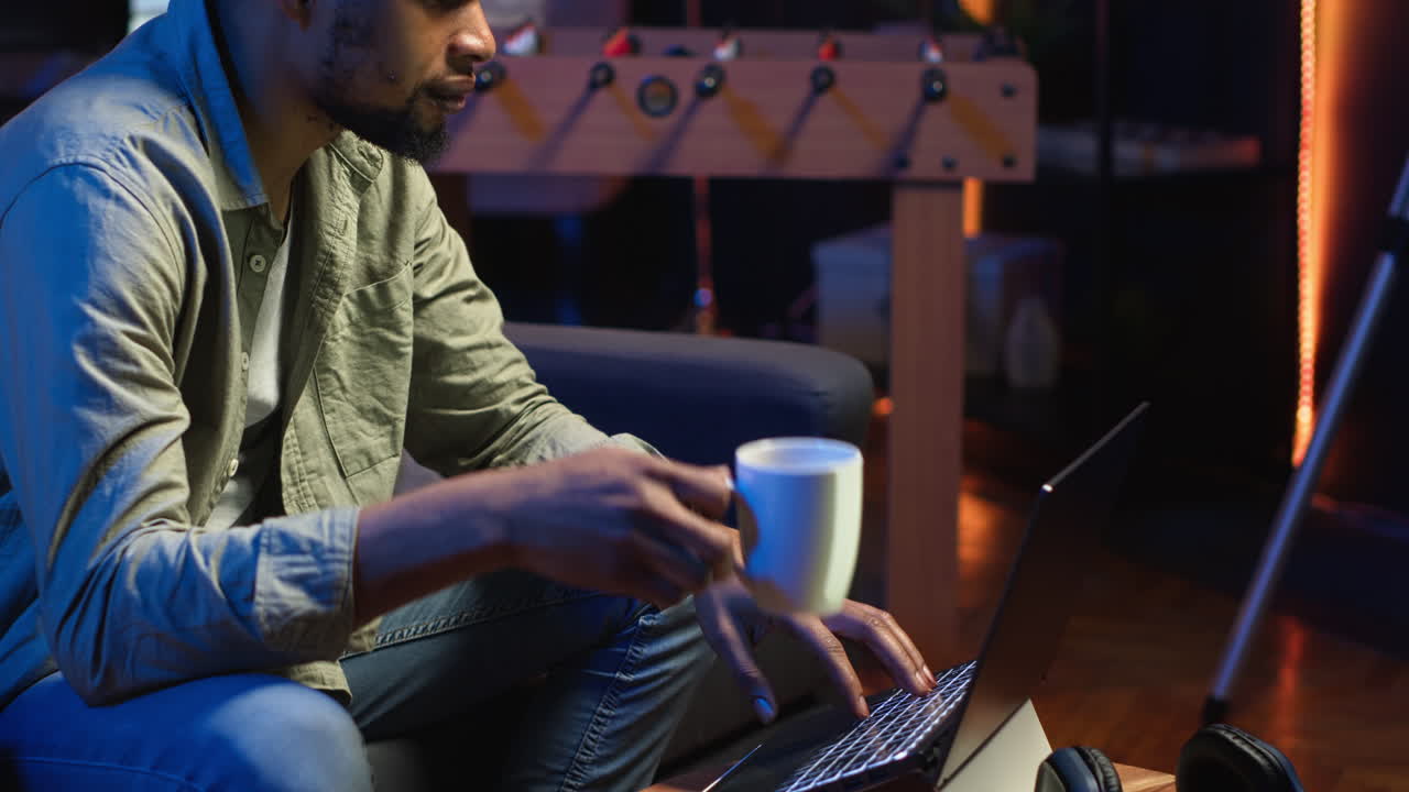 Vertical Video African American young adult working remotely on a laptop under loft neon lights