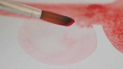 detail eines pinsels, der rote aquarelle malt