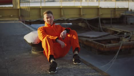 Retrato-De-Un-Joven-Trabajador-Con-Uniforme-Naranja-Sentado-Durante-Su-Descanso-Junto-Al-Mar