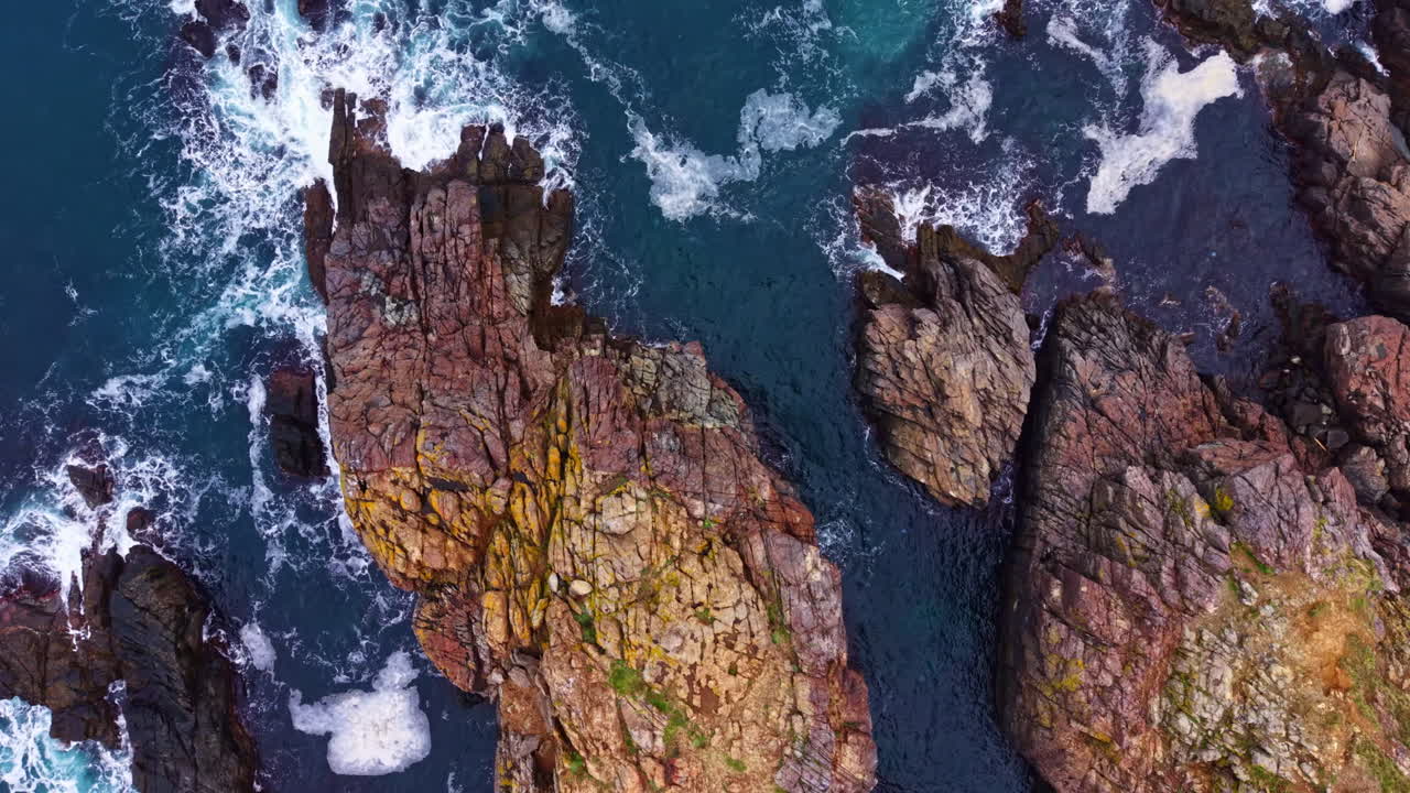 Scogliere costiere incontrano rocce frastagliate e onde che si infrangono sotto un cielo azzurro all'alba, in un sereno paesaggio marittimo
