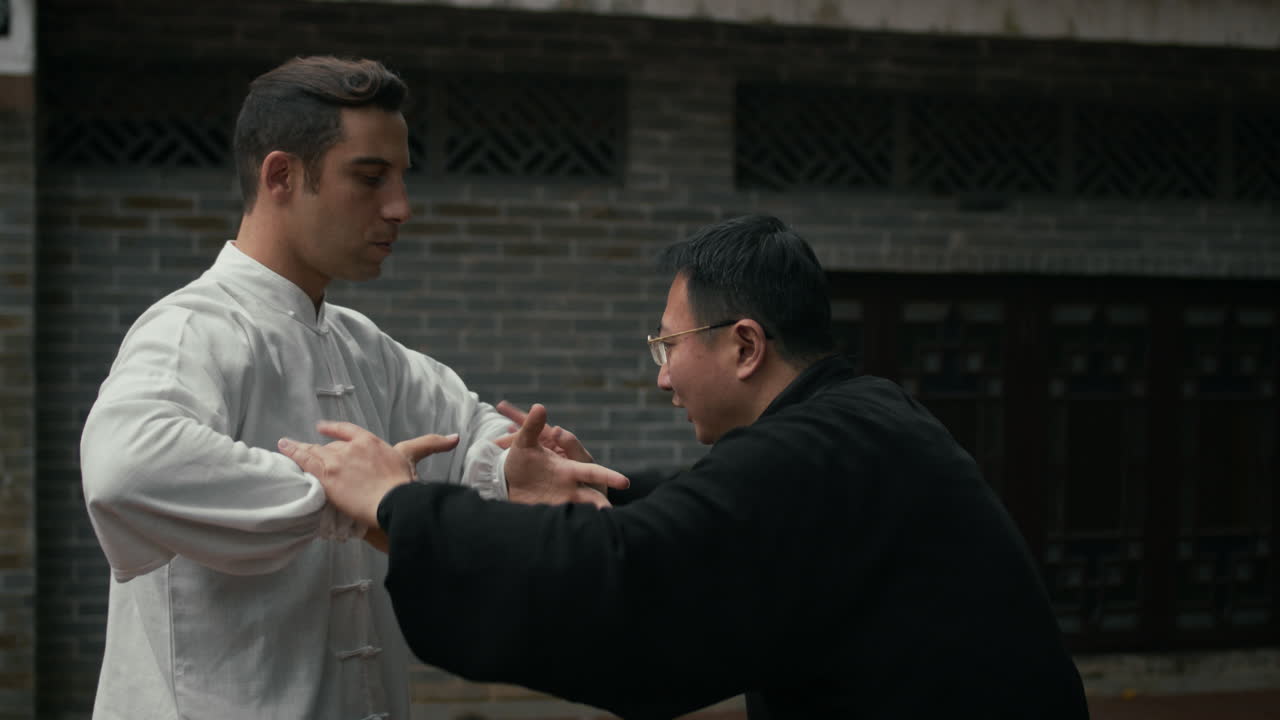Two men practicing martial arts, likely Tai Chi or Push Hands, in a traditional outdoor setting
