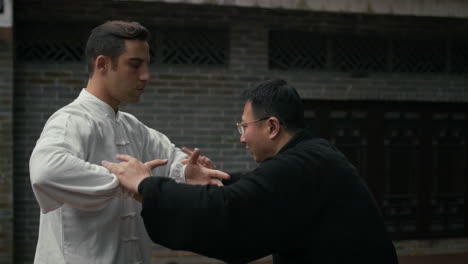 two men practicing martial arts, likely tai chi or push hands, in a traditional outdoor setting