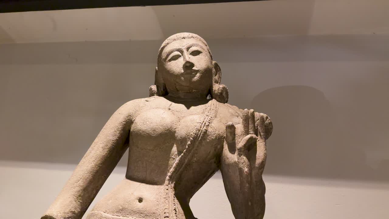 Camera slowly pans across ancient Buddhist stone statue under soft indoor lighting in Bangkok museum