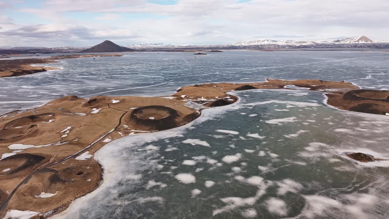 Aerial view over Skútustaðagígar pseudo craters in Mývatn near Reykjahlíð, Iceland, with frozen lake patches, volcanic shapes, and a surreal Arctic landscape under soft winter light.