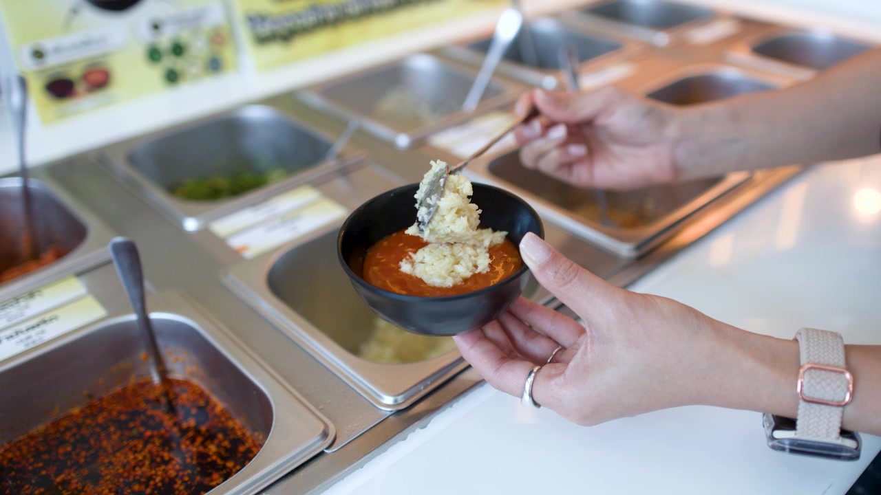 Mano che aggiunge aglio tritato a una ciotola di salsa in una stazione di condimenti self-service