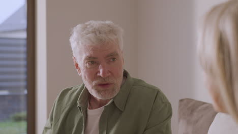 portrait of senior man drinking tea and talking with someone while sitting on sofa at home