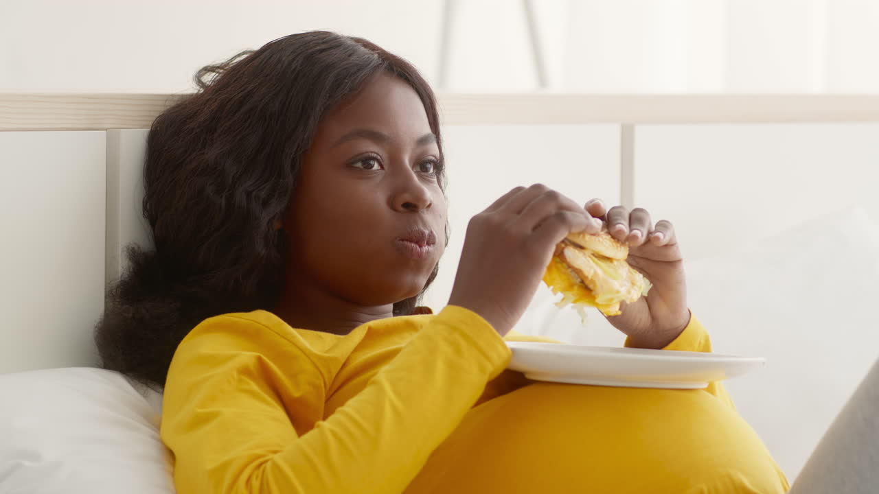 Donna incinta che mangia un hamburger a letto