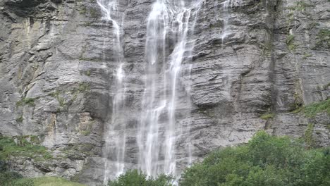 giant waterfall over the rocks falling down on a bright day in lauterbrunnen in switzerland between the green trees. slowmotion shot.