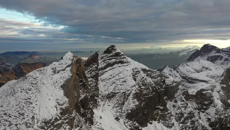 aerial shot moving slowly to the right, focusing on the high peaks of the swiss mountains with a big and dramatic cloud from a storm in the background