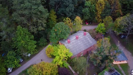 antena de arriba hacia abajo sobre una casa moderna escondida entre coloridos bosques otoñales durante el día, autos estacionados