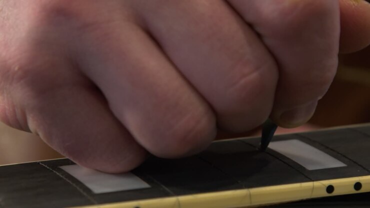 Tecnico in primo piano che usa un cutter di precisione per pulire le fessure dei tasti su una chitarra elettrica.