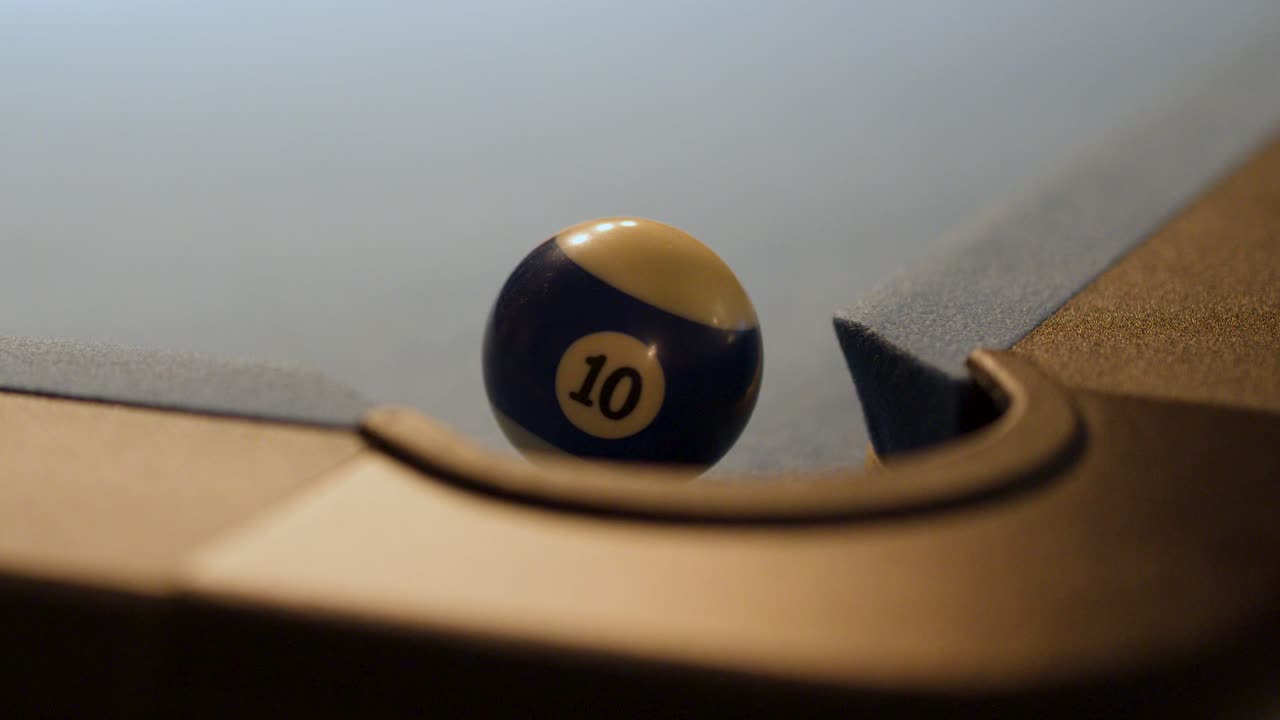 Number 10 billiard ball rolls into corner pocket on blue felt table, low warm lighting