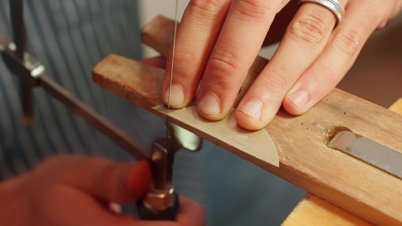 An artisan saws through a piece of wood while holding it, showcasing precision and artistry involved in woodworking.