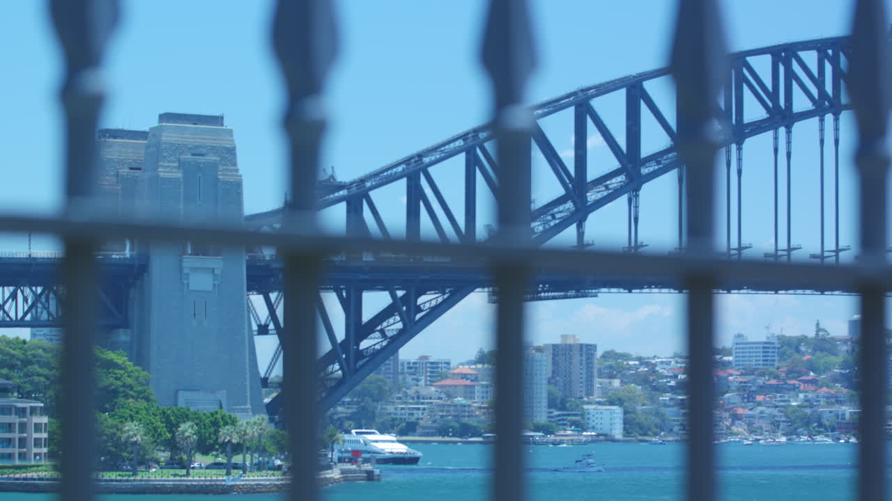 Pan up through a fence to reveal the Sydney Harbour Bridge on a clear sunny Blue Sky Day