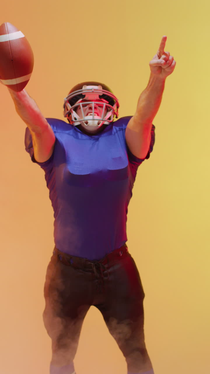 video vertical de un jugador de fútbol americano caucásico masculino sosteniendo la pelota, con iluminación naranja de neón