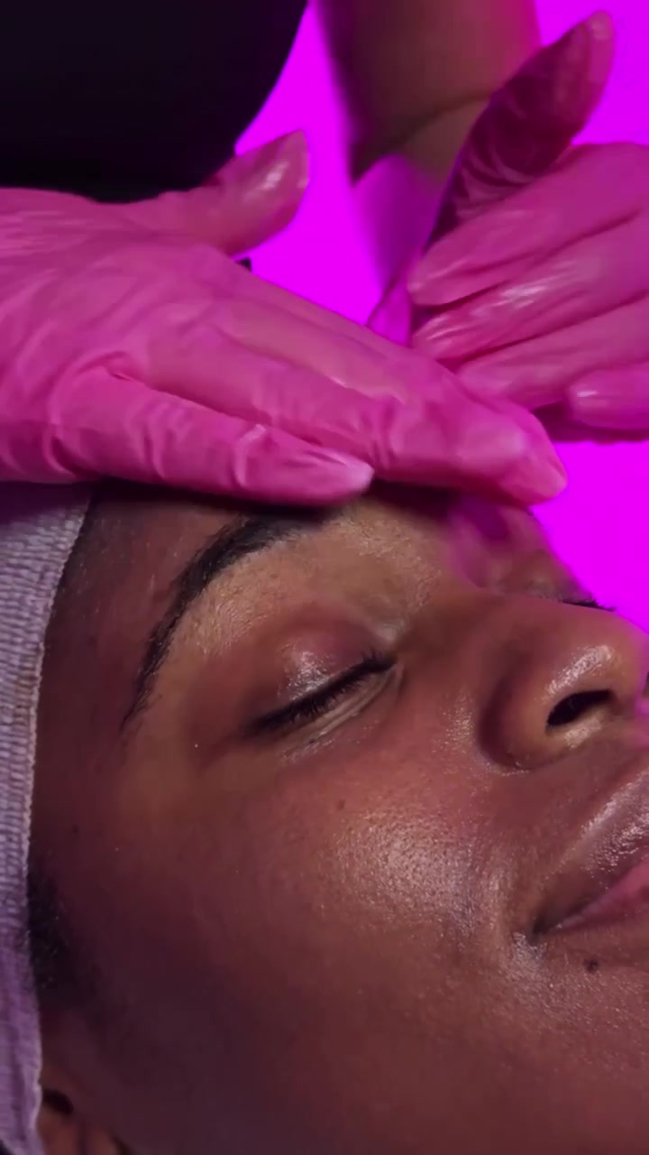 Femme recevant un soin du visage dans un institut de beauté, avec des lumières vives et colorées en arrière-plan, en soirée.