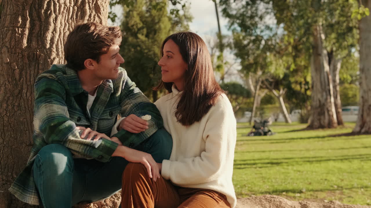 Happy young partners man and woman relaxing sitting in park under tree