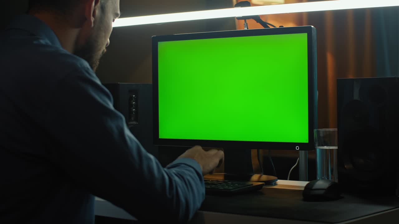 un hombre trabaja frente a una computadora con una pantalla verde.