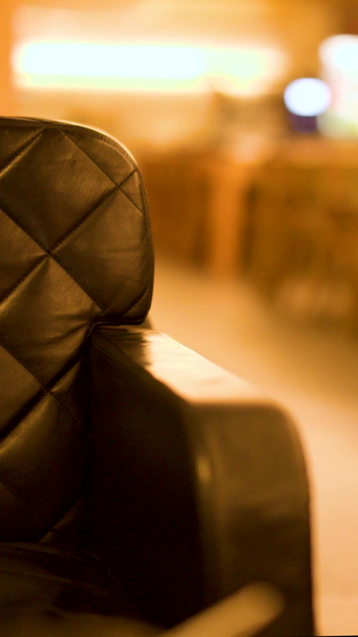 A person exits frame, leaving a black leather chair in a warmly lit airport lounge