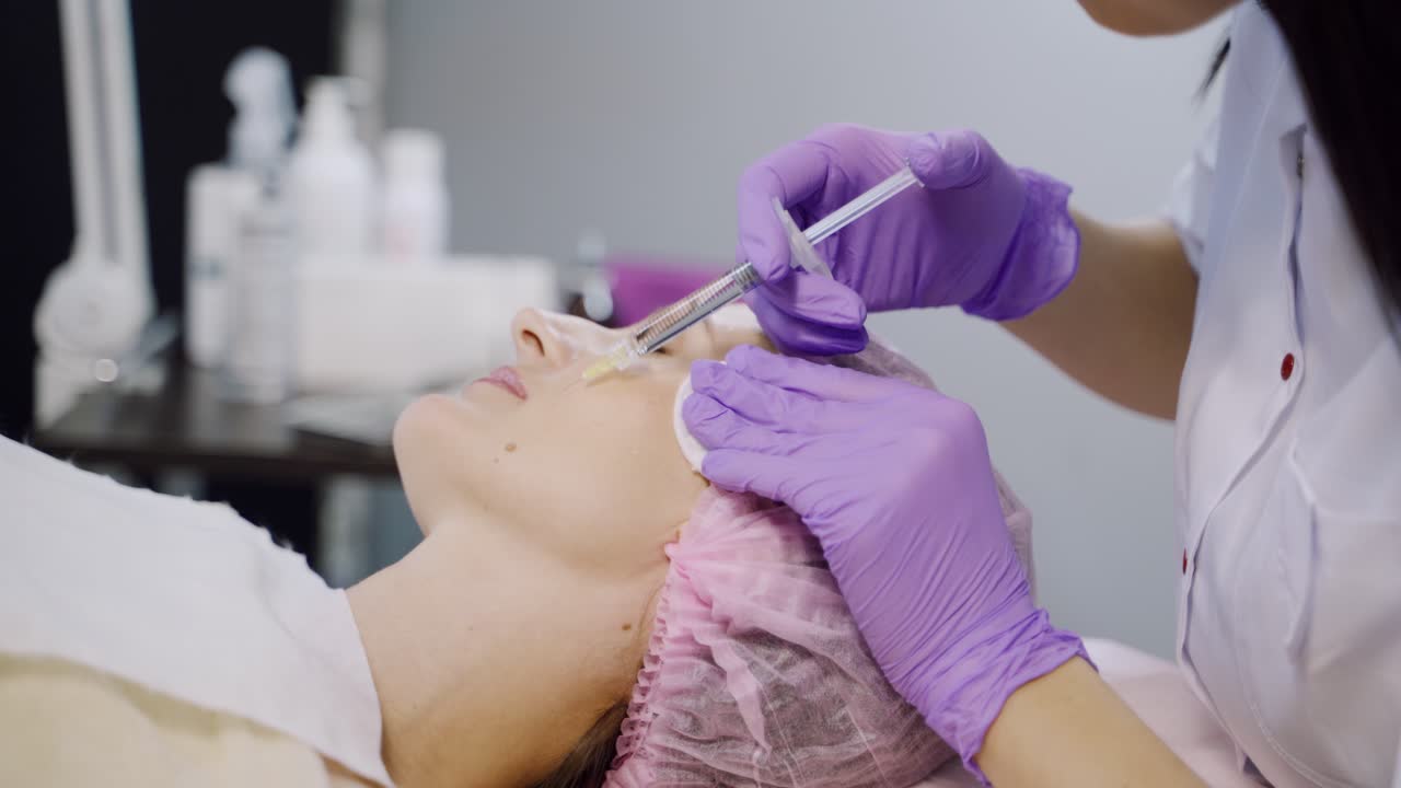 A client is undergoing mesotherapy in the beauty salon using injections on the background of different cosmetics. Beauty industry.
