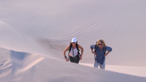 pareja con mochila subiendo a la duna de arena 4k