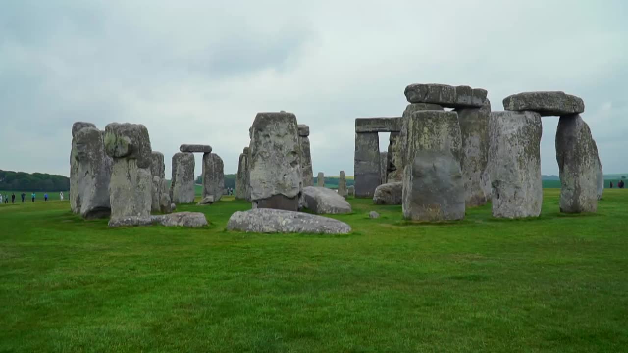 Slow motion clip of Stonehenge, showcasing the massive prehistoric stone circle monument on the green plains of Salisbury, England, under cloudy skies.