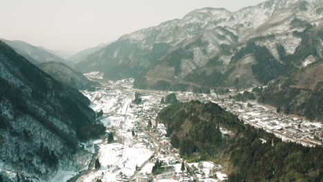 vista panorámica de una ciudad en nieve profunda con imponentes montañas forestales en okuhida hirayu, gifu, japón