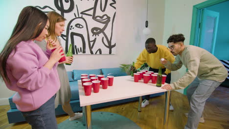 happy multiethnic young friends playing beer pong at home