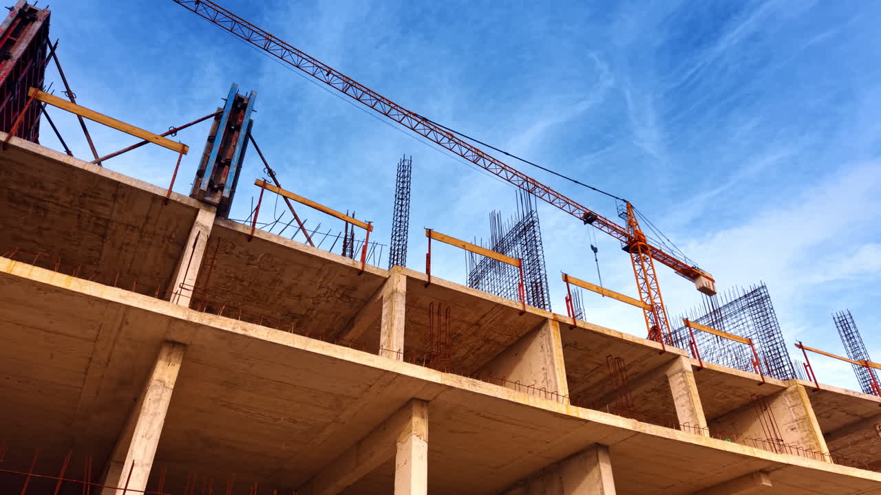 Construction of a multi-storied building with metal armature on the top. Yellow crane towers above the structure. Low angle view