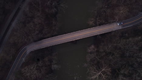 aerial: car drives over narrow bridge at dusk