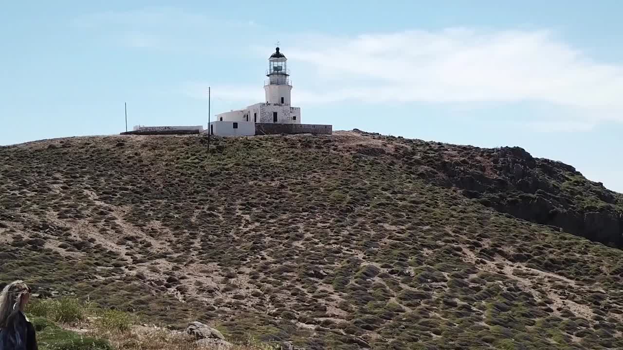 drone aéreo moviéndose hacia atrás revelando mujer faro mykonos grecia