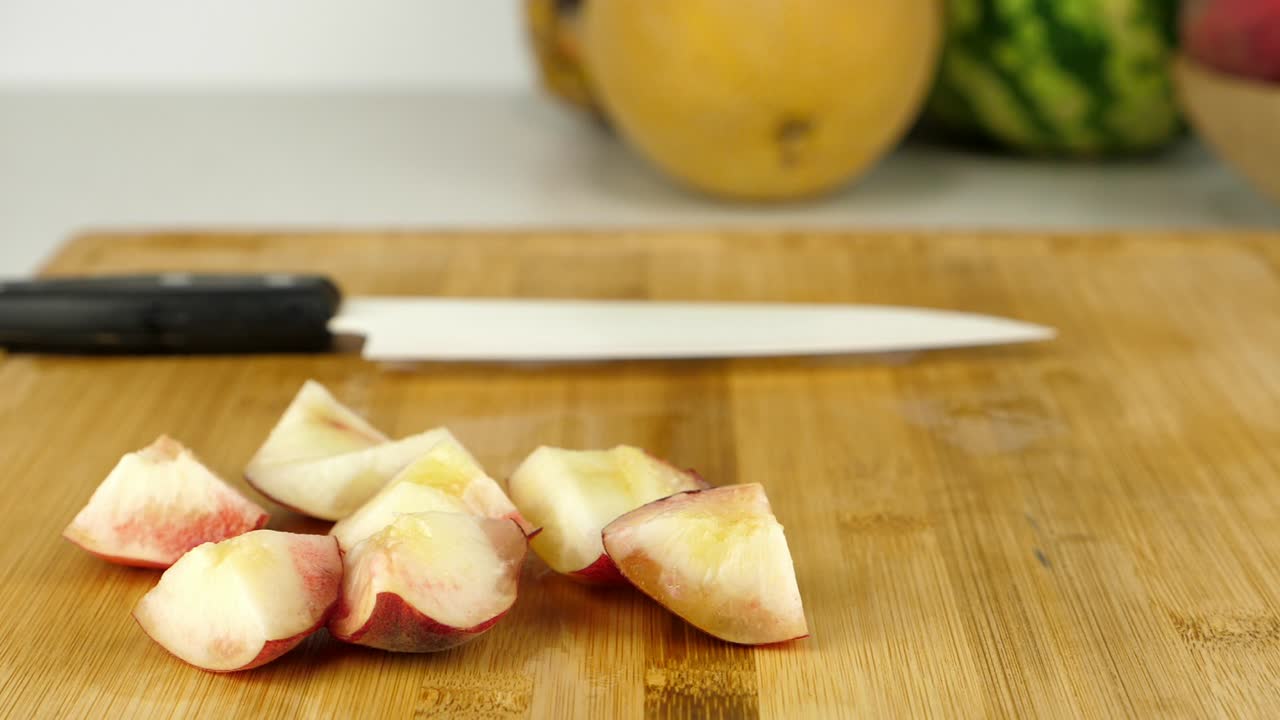 Carrellata di pezzi di frutta su un tagliere di bambù, con un coltello in ceramica e vari frutti esotici sullo sfondo