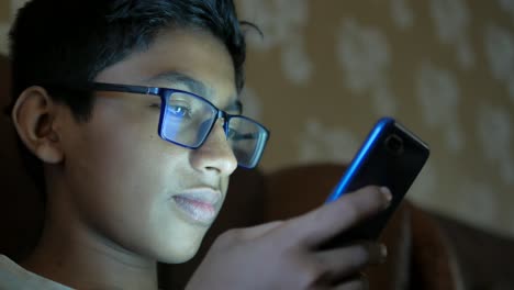 Teenage-boy-sitting-on-sofa-using-smart-phone-at-night