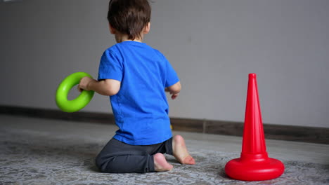 charming baby boy in blue t-shirt sits on the floor at home. energetic toddler plays with a pyramid.
