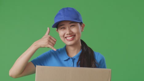 푸른 유니폼을 입은 아시아 여성 택배사의 클로즈업은 스튜디오에서 녹색 화면 배경에 상자를 배달하는 동안 제스처와 웃음을 보여줍니다.